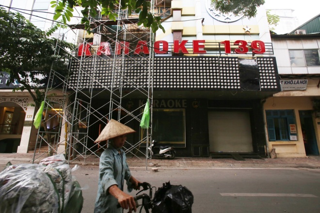 Phố Triệu Việt Vương (Hoàn Kiếm), người phụ nữ làm nghề mua bán phế liệu chờ mua những mảnh nhựa tháo ra từ tấm biển quảng cáo khổ lớn tại một quán hát.